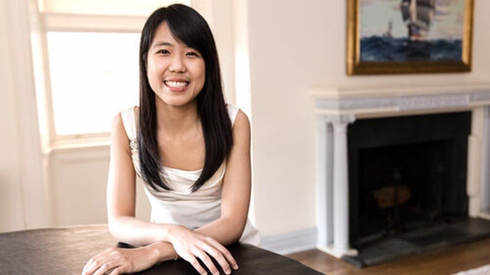 Photo of Kate Liu, sitting at the table. A window and a fireplace with a picture above it in the background.