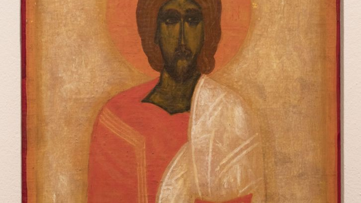 An icon with a painted image of a saint, with an orange halo around his head. The figure is wearing an orange and golden robe, carrying a manuscript.