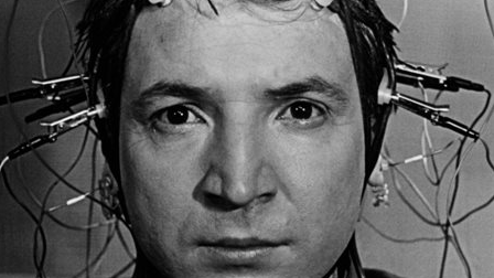 The face of a man with cables attached to his head. Black and white picture.