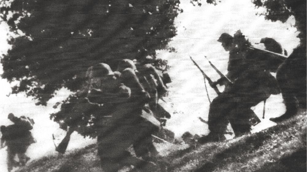 Czarno-biała fotografia żołnierzy maszerujących po zboczu.