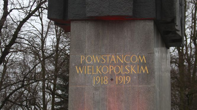 Żołnierze w historycznych mundurach stoją wokół pomnika poświęconego Powstańcom Wielkopolskim.