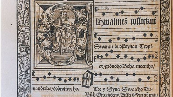 Karta średniowiecznej księgi z zapisem gotycką czcionką i ozdobnym inicjałem.