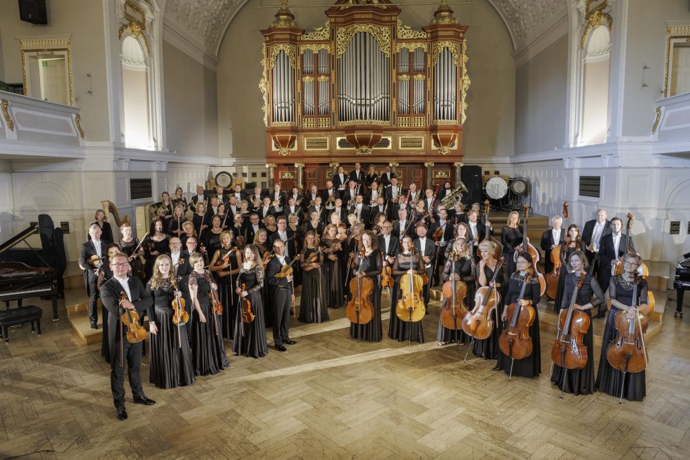 Orkiestra Filharmonii Poznańskiej, fot. Piotr Skórnicki Muzycy orkiestry pozują z instrumentami na tle organów w Auli UAM.