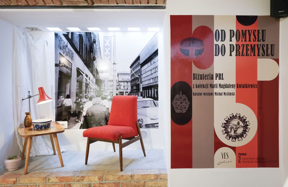 Po prawej plakat reklamujący wystawę, po lewej stolik i fotel z okresu PRL na tle czarno-białej fotografii ulicy dużego miasta. - grafika artykułu