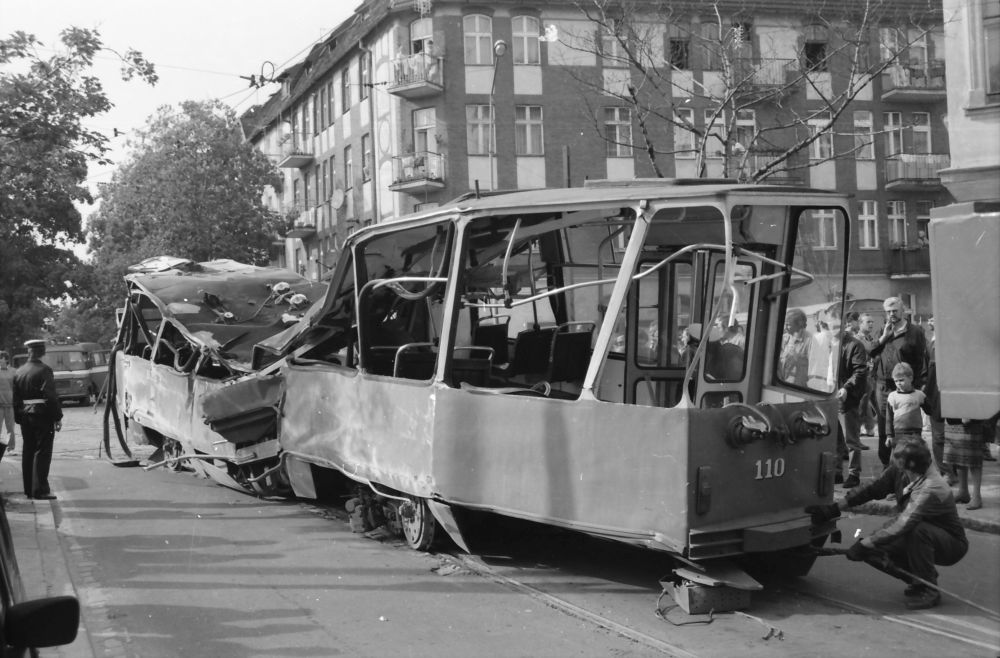 Czarno-białe zdjecie, na którym wokół wraku tramwaju zbierają się mieszkańcy Poznania. Po jednej stronie stoi policjant. - grafika artykułu