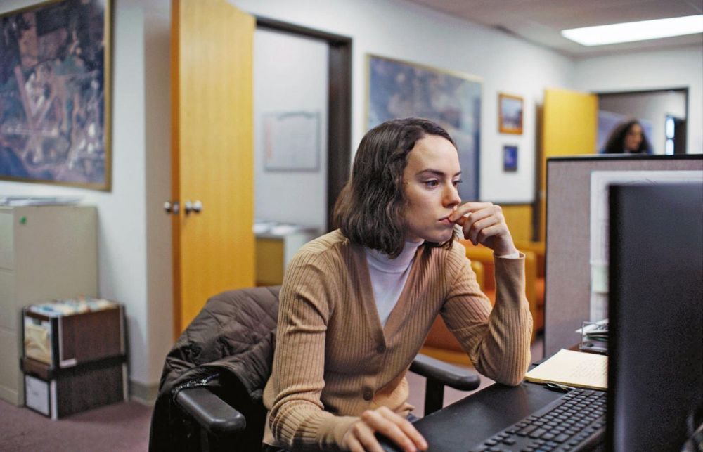 Młoda dziewczyna w białym golfie i beżowym swetrku siedzi przy biurku, pochyla się w stronę komputera. - grafika artykułu