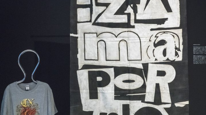 Czarno-biały plakat zespołu Pidżama Porno na ścianie i wisząca na manekinie krawieckim niebieska koszulka z nadrukiem przedstawiającym ludzkie serce.