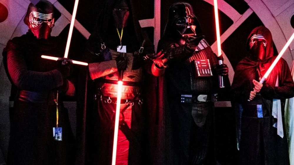 Cztery postacie znane z uniewersum "Star Wars" pozują w czarnych kostiumach i świecącymi mieczami świetlnymi, promując specjalną strefę na Pyrkonie.