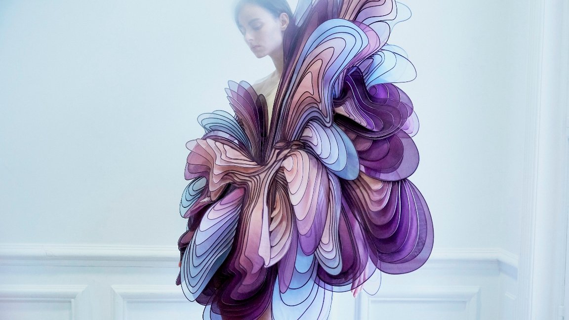 A photo of a woman dressed in blue, purple and pink cloth which looks like many butterfly's wings. White background - grafika artykułu