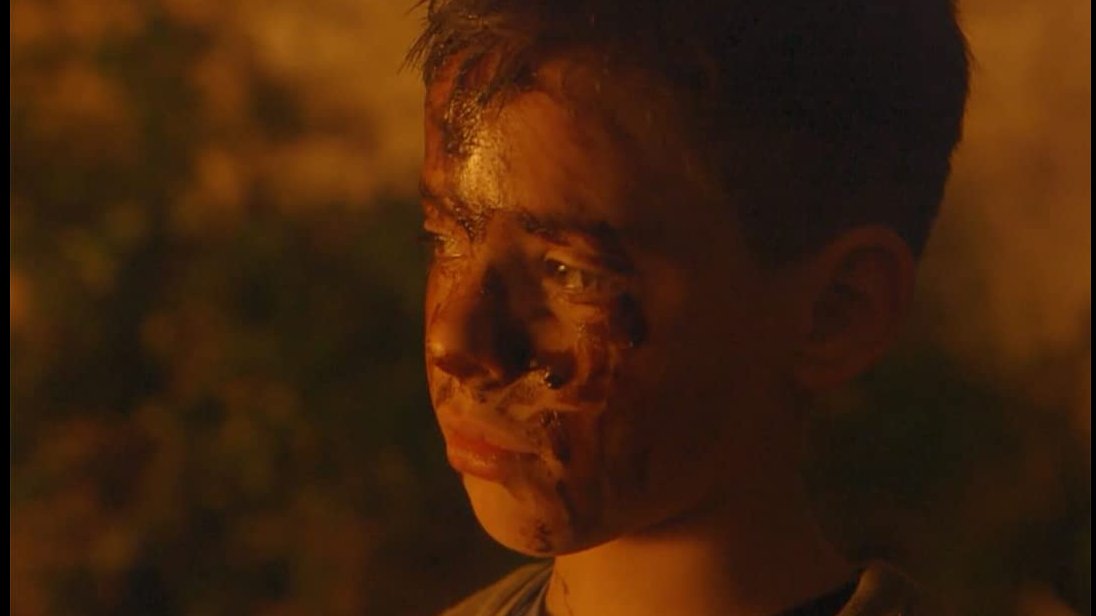 A shot from a movie: photo of a boy's dirty face who is looking into the distance with sorrow.