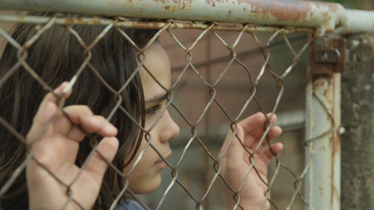 Photo from the movie: a girl standing by the metal fence, holding it and looking somewhere