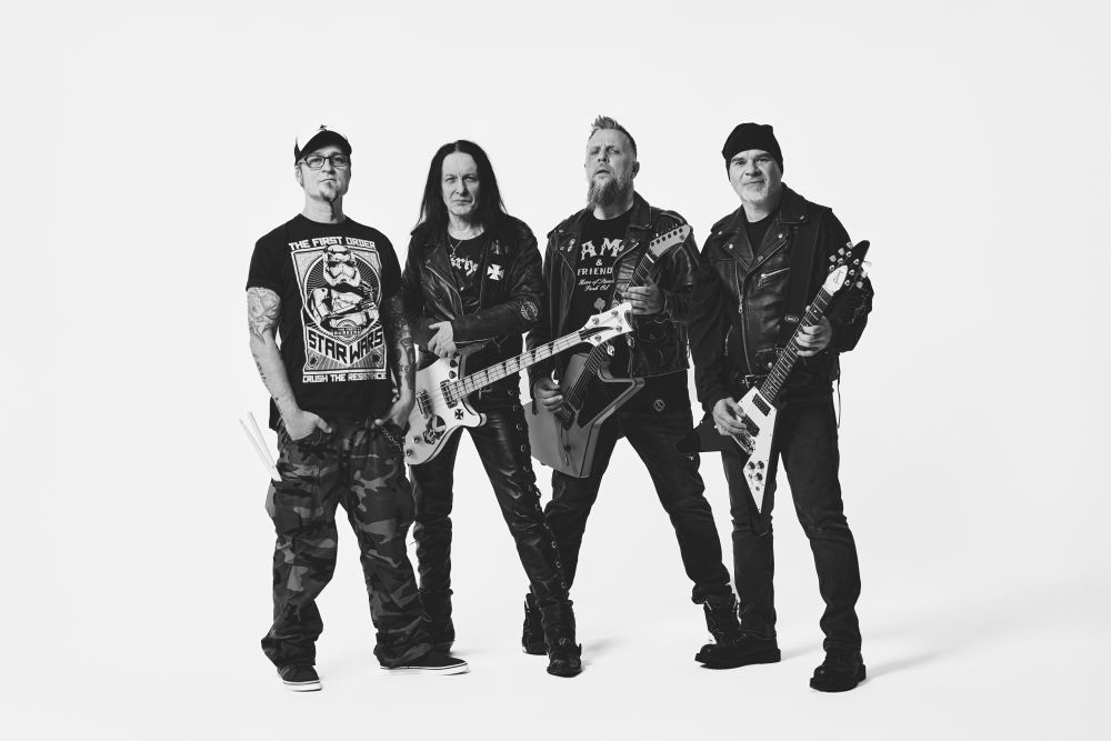 Black and white photo of the Acid Drinkers members. Four men who are standing, three of them are holding electric guitars.