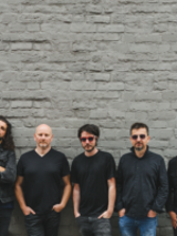 Photo of the band - five men standing by the wall