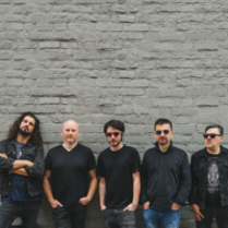 Photo of the band - five men standing by the wall