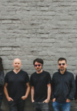 Photo of the band - five men standing by the wall