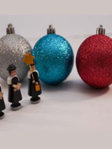 Picture of three Christmas balls (silver, blue and red) and three small figures of carollers.