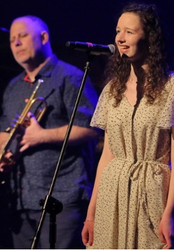 Photo of the performers: young woman singing to a microphone and a man holding a trumpet in his hands.
