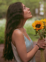 Photo of the artist holding sunflowers in her hands.