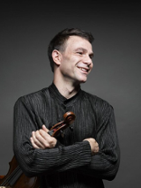 Photo of the artist, Amihai GROSZ, who is holding the violin in his hand