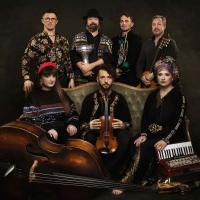 Photo of the band: seven people, three of them sitting on a sofa.