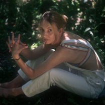Photo of a young girl sitting on ground. Green leaves as a background.