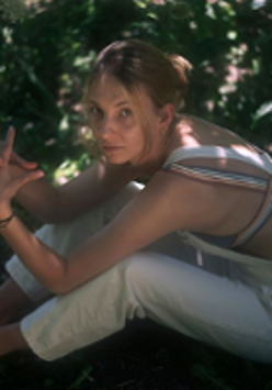 Photo of a young girl sitting on ground. Green leaves as a background.