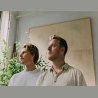 A photo of two men standing next to each other, looking to the side.