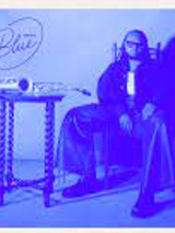 Picture in blue colours of Immanuel Wilkins sitting on a chair at a small table.