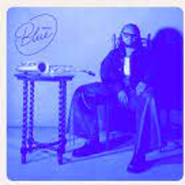 Picture in blue colours of Immanuel Wilkins sitting on a chair at a small table.