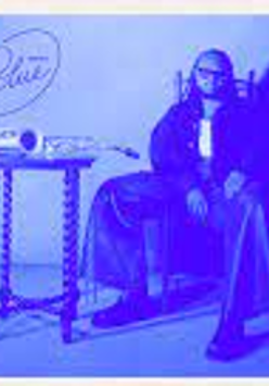 Picture in blue colours of Immanuel Wilkins sitting on a chair at a small table.