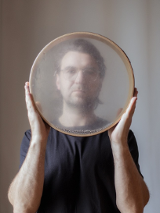 Picture of Krzysztof Dysa - a man holding a round object tat looks like a tambourine in front of him.