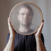 Picture of Krzysztof Dysa - a man holding a round object tat looks like a tambourine in front of him.