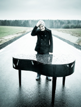 Photo of the artist - a young man standing by the piano on the road.