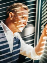 Photo of Michał Bajor, who is looking out of the window, through blinds.