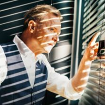 Photo of Michał Bajor, who is looking out of the window, through blinds.