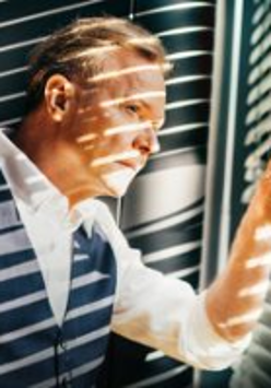 Photo of Michał Bajor, who is looking out of the window, through blinds.
