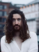 Photo of the singer - young, long-haired man in white shirt.