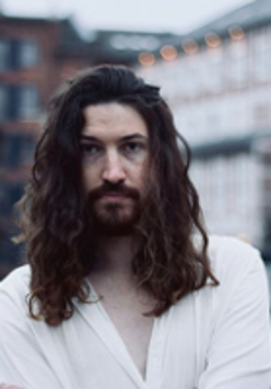 Photo of the singer - young, long-haired man in white shirt.