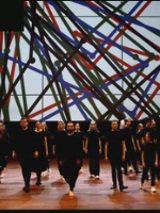 Photo of a group of people dressed black on stage. A colourful visualization in the background.