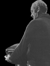 Gray silhouette of a man playing the accordion; black background.