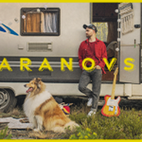 Photo of a man who is leaning against a caravan and looking his right. In front of him - a collie dog.