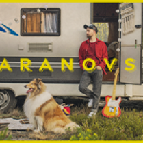 Photo of a man who is leaning against a caravan and looking his right. In front of him - a collie dog.