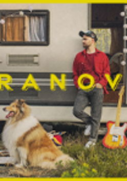 Photo of a man who is leaning against a caravan and looking his right. In front of him - a collie dog.