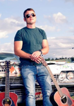 Photo of Rodney Branigan - a young man sitting on a car's bonnet, with two guitars on his left and right.