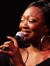 Picture of the artist, who holds a microphone in her hand.