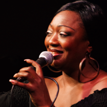 Picture of the artist, who holds a microphone in her hand.