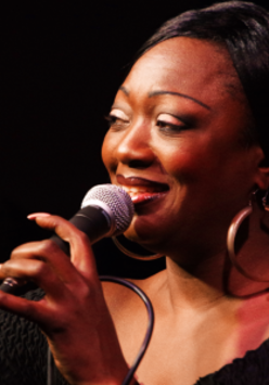 Picture of the artist, who holds a microphone in her hand.