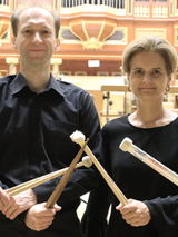 Two musicians (a man and a woman) holding drumsticks in their hands. The pipe organ in the background.