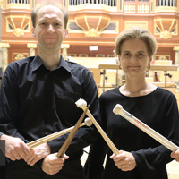 Two musicians (a man and a woman) holding drumsticks in their hands. The pipe organ in the background.