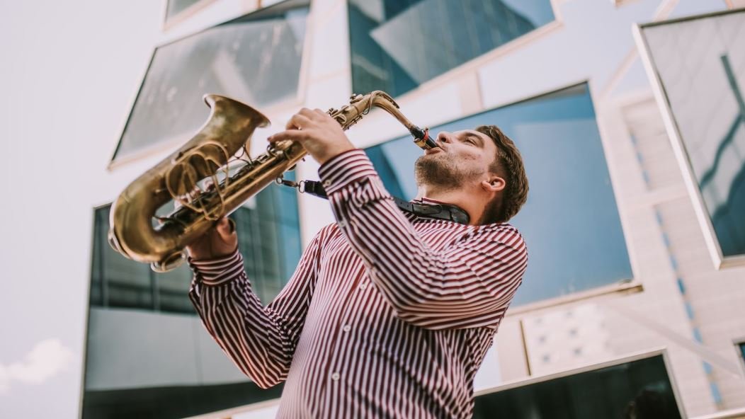 Photo of Dawid Tokłowicz playing the saxophone. Several mirrors in frames hanging behind the musician.